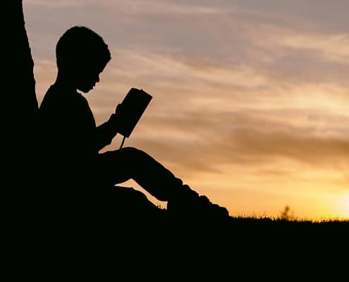 Child reading the Bible against a tree.